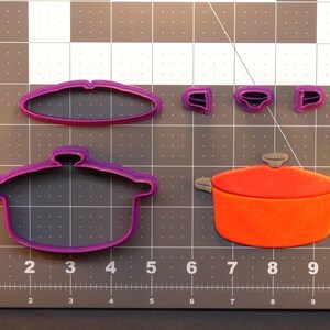 May include: A set of purple plastic cookie cutters in the shape of a pot with a lid, a pot without a lid, and three separate pot handles. The cutters are on a gray cutting mat with white markings.