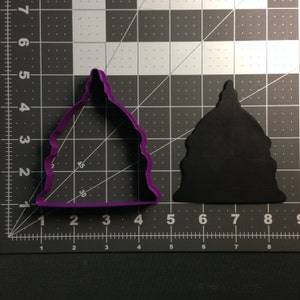 Puede incluir: Cortador de galletas de plástico morado con forma del Capitolio de los Estados Unidos. El cortador está sobre una superficie de rejilla blanca y negra.