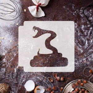 May include: White plastic stencil of a snake with a coiled body and raised head on a brown surface covered in white flour.