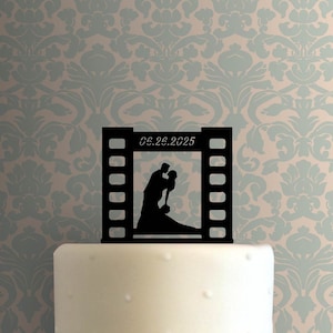 May include: Black silhouette of a couple kissing inside a film strip frame with the date 06.26.2025. This is a cake topper for a wedding.