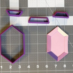 May include: A set of five purple plastic cookie cutters shaped like a hexagon, a rectangle, and two smaller rectangles, and a pink and purple gem.
