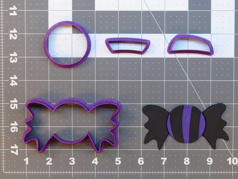 May include: A set of four purple plastic cookie cutters. The cutters are shaped like a candy, a bow, and two half circles.