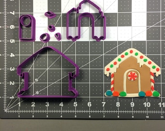 May include: A set of purple plastic gingerbread house cookie cutters. The set includes a large gingerbread house, a small gingerbread house, a candy cane, a door, and a window.