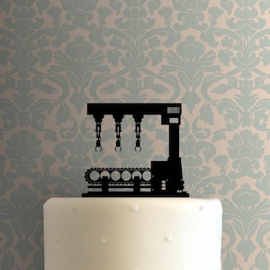 May include: Black silhouette of a factory conveyor belt with three robotic arms, a cake topper.