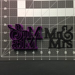 May include: Two cookie cutters, one purple and one black, with the words "Mr & Mrs" and "Mr & Mrs" in a stylized font.