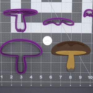 May include: Four purple plastic cookie cutters shaped like mushrooms. The cutters are on a gray grid background. One cutter is a simple mushroom shape, another is a mushroom with a detailed cap, and the last two are half-circle shapes.