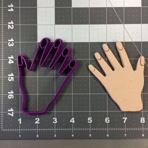 Pode incluir: Dois cortadores de biscoitos de plástico roxo em forma de mão, um com um contorno detalhado e o outro com uma superfície lisa.