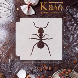 May include: A white plastic stencil of an ant, measuring 5 inches wide and 5 inches tall. The stencil is on a brown surface with a ruler and other baking supplies.