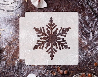 May include: A white snowflake stencil on a brown surface with flour scattered around it. The stencil is made of plastic and has a snowflake design cut out of it.