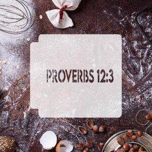 May include: A square, off-white plastic stencil featuring the text "PROVERBS 12:3" in a bold, dark, stencil-style font. The stencil has small tabs on the sides and is designed for decorative applications on surfaces like cakes or baked goods.