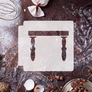 Puede incluir: Un esténcil con un diseño de mesa, ideal para hornear o manualidades. La mesa marrón tiene una parte superior rectangular y patas ornamentadas. El esténcil está sobre un fondo blanco, rodeado de harina e ingredientes para hornear.