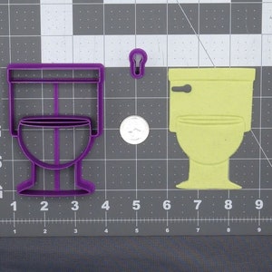 May include: A purple plastic toilet-shaped cookie cutter, a toilet-shaped cookie, and a small keyhole-shaped cutter. The cookie cutter is approximately 4 inches tall. The cookie is light yellow. The items are on a gray cutting mat.