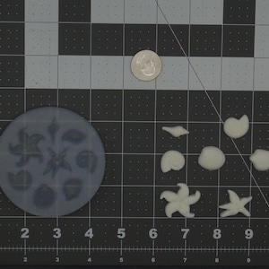May include: A silicone mold with eight different shapes of seashells and starfish. The mold is light gray and the shapes are raised.