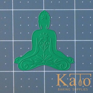 May include: Green plastic cookie cutter shaped like a meditating Buddha with intricate floral designs.