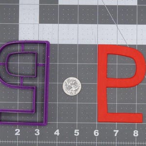 Könnte beinhalten: Zwei Ausstecher, einer in Form des Buchstabens "P" in Rot und der andere in Form des Buchstabens "9" in Lila. Die Ausstecher befinden sich auf einem grauen Gitterhintergrund.