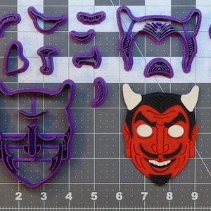 May include: A set of purple plastic cookie cutters in the shape of a devil's face. The set includes a full face, horns, eyes, nose, mouth, and eyebrows. There is also a red plastic devil mask.