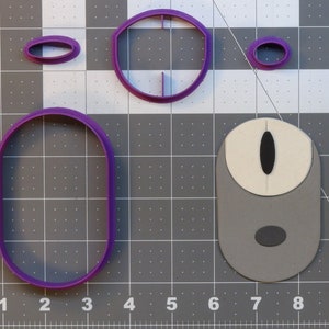 May include: A collection of purple plastic cookie cutters in various oval shapes, including a large oval, a smaller oval, and two other oval shapes. A gray and white mouse-shaped item is also present.