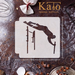 May include: White plastic stencil of a person doing a high bar exercise. The stencil is 12.7 cm wide and 12.7 cm tall. The stencil is on a brown surface with a ruler and other baking supplies.