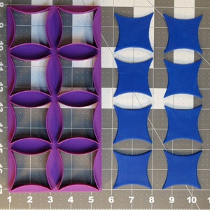 Puede incluir: Un juego de cortadores de galletas de plástico morado y azul. El cortador morado tiene un patrón repetitivo de formas de trébol de cuatro hojas. Los cortadores azules tienen forma de estrellas de cuatro puntas.