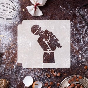 May include: A white stencil with a raised fist holding a microphone. The stencil is on a brown surface with flour scattered around it.