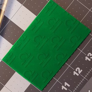 May include: A green plastic sheet with a repeating pattern of the Libra zodiac symbol embossed on the surface.