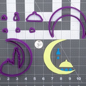 Peut inclure: Un ensemble d'emporte-pièces en plastique violet en forme de croissant de lune, de mosquée et de dôme. Les emporte-pièces sont sur un fond de grille grise.