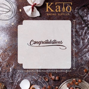 Pode incluir: Estêncil de plástico branco com a palavra "Parabéns" escrita em itálico. O estêncil está sobre uma superfície marrom com farinha e outros utensílios de confeitaria.