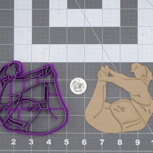 May include: Two purple and brown plastic cookie cutters shaped like people in yoga poses. The cutters are on a gray and white grid background.