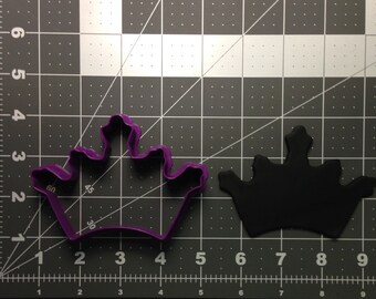 May include: Purple plastic crown cookie cutter with a black plastic crown cookie cutter in the background.