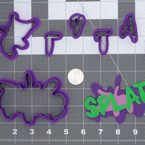 May include: Purple plastic cookie cutters in various shapes, including letters, a splat, and a star. The cutters are on a gray grid background.