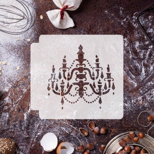 May include: A white stencil of a decorative chandelier with a detailed design. The stencil is on a brown surface with flour scattered around it.