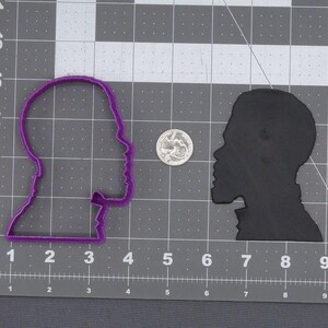 May include: Two silhouette cookie cutters, one purple and one black, in the shape of a person's head. The cutters are on a gray grid background.