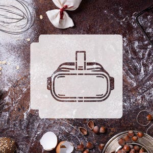 May include: A white stencil with a black outline of a virtual reality headset on a brown surface covered in white flour.