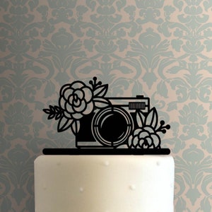 May include: Black silhouette of a camera with floral accents, a wedding cake topper.