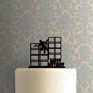 May include: Black silhouette cake topper of a person in a window washing lift with the words "Happy Birthday" below.