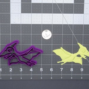 Peut inclure: Deux emportes-pièces en plastique en forme de ptérodactyles. L'emporte-pièce de gauche est violet et celui de droite est jaune.