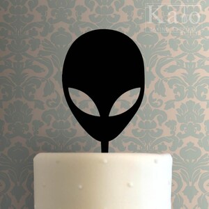 Pode incluir: Topo de bolo de cabeça de alienígena preto. O alienígena tem olhos grandes e uma cabeça redonda. O topo é feito de acrílico e é perfeito para uma festa com tema espacial.