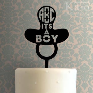 May include: Black silhouette of a baby pacifier with the text "ABC it's a BOY" and a circle with the letters "ABC" in it. The pacifier is on a white cake.