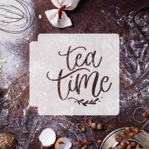 May include: A square stencil with the words "tea time" in a decorative script, surrounded by baking ingredients. The image includes flour, hazelnuts, and a whisk, suggesting a baking theme.