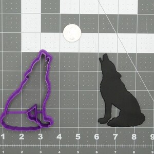 Puede incluir: Cortador de galletas de plástico morado en forma de lobo aullando a la luna. El cortador está sobre un fondo de rejilla gris.