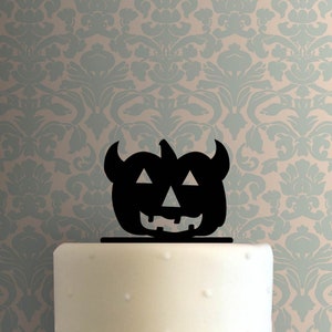 Puede incluir: Silueta negra de una calabaza con cuernos y una cara de miedo. La calabaza está encima de un pastel blanco.