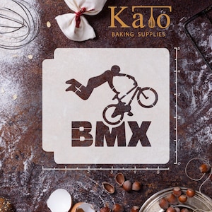 May include: White plastic stencil with a silhouette of a person riding a BMX bike and the word "BMX" underneath. The stencil is on a brown surface with a ruler marked in inches.