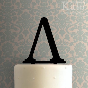 May include: Black acrylic cake topper shaped like the Greek letter lambda. The topper is sitting on top of a white cake.