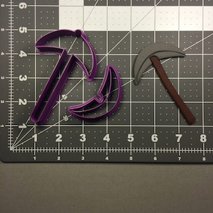May include: Two cookie cutters, one purple and one gray, shaped like a pickaxe.