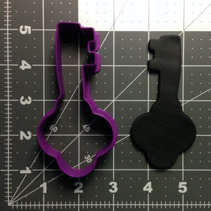 Puede incluir: Cortador de galletas de plástico morado en forma de llave con un recorte de fondant negro de la misma forma.