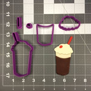 May include: Purple plastic cookie cutters in the shape of a milkshake, a cup, a straw, and a whipped cream topping. The cutters are on a gray grid background.