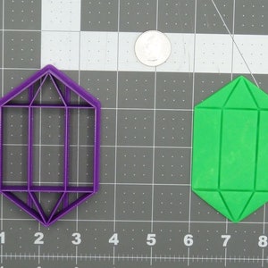 May include: Two plastic cookie cutters shaped like a gem. The cutter on the left is purple and the cutter on the right is green.
