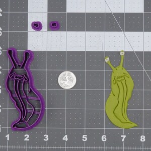 May include: Two cookie cutters shaped like slugs. One is purple and the other is green. Both have eyes and a mouth.