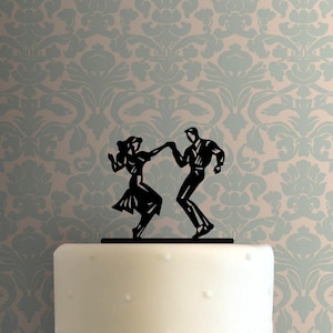 Peut inclure: Silhouette noire d'un couple dansant sur un gâteau blanc. Le couple est dans une pose classique des années 1950, la femme en robe et l'homme en costume.