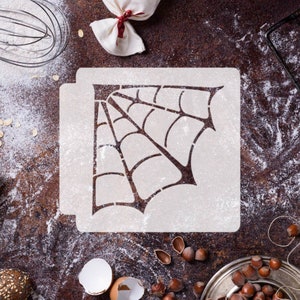 Peut inclure: Un pochoir en plastique blanc avec un motif de toile d'araignée. Le pochoir est sur une surface brune avec de la farine éparpillée autour.